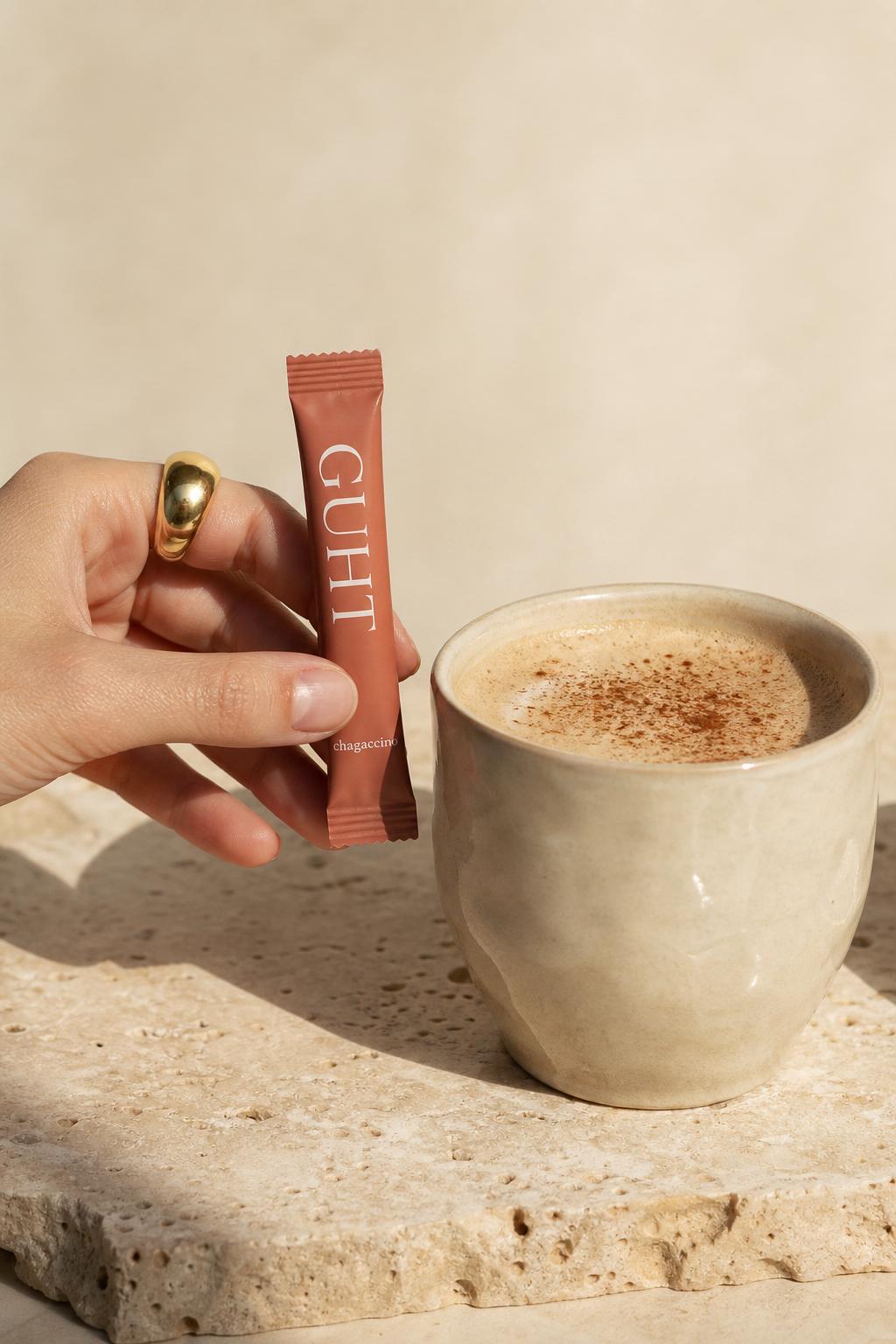 Hand tearing open a Guht Chagacchino sachet over a frothy oat milk latte